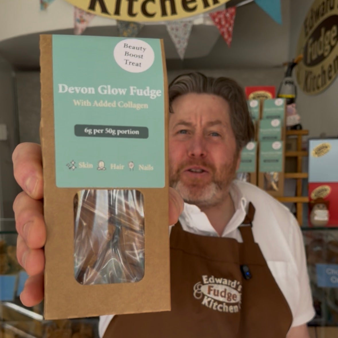 Person wearing a brown apron holding a box of fudge with 'Edward's Fudge Kitchen' branding.