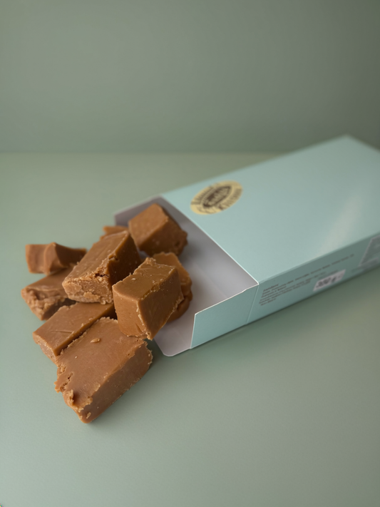Open box of ginger fudge with pieces spilling out on a light green surface.