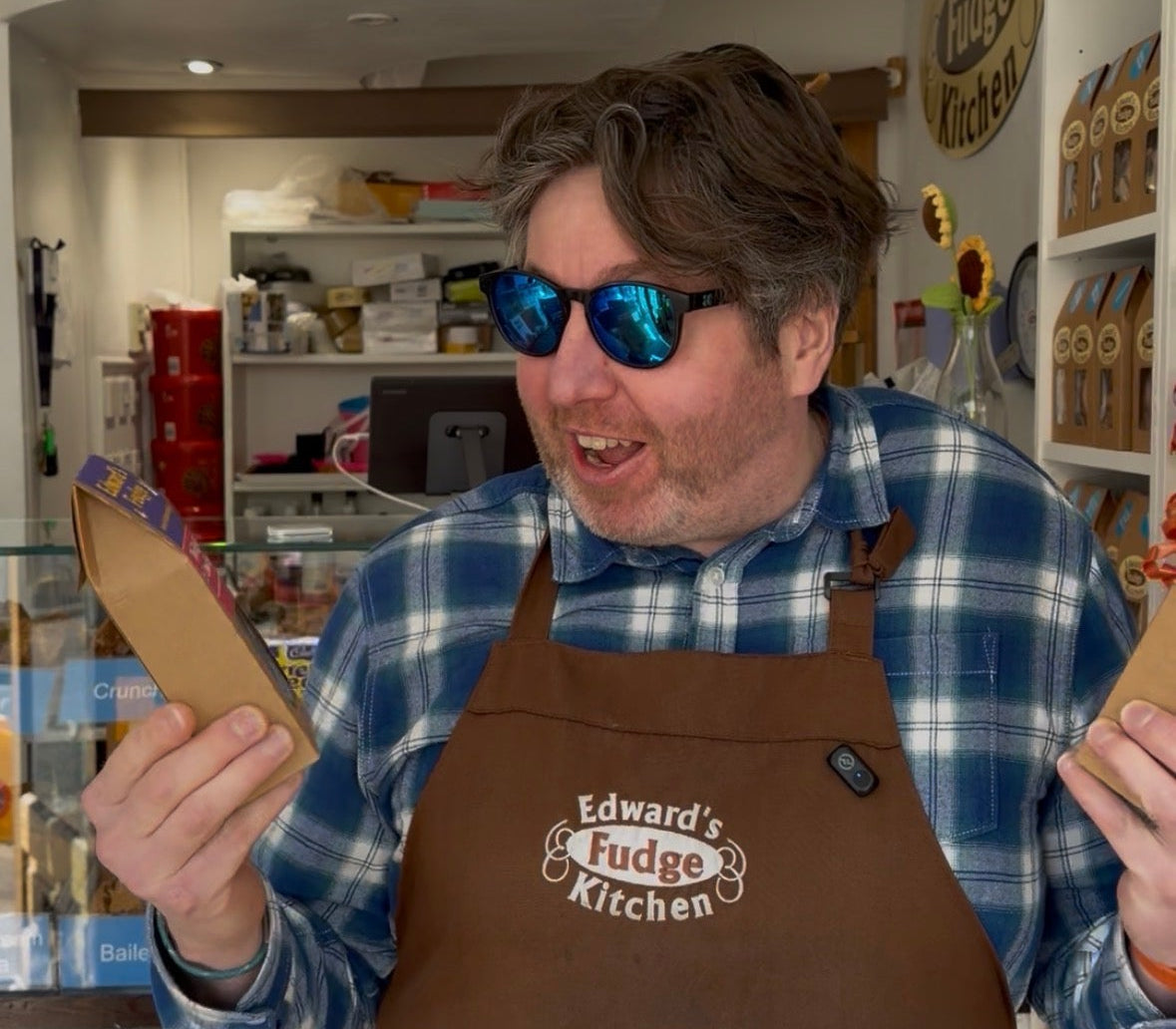 Person wearing a brown apron with 'Edward's Fudge Kitchen' logo in a store setting.